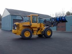 Yellow skid loader with bucket raised, in parking lot