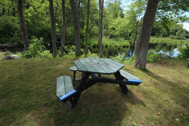 Green octagonal bench surrounded by trees by water feature